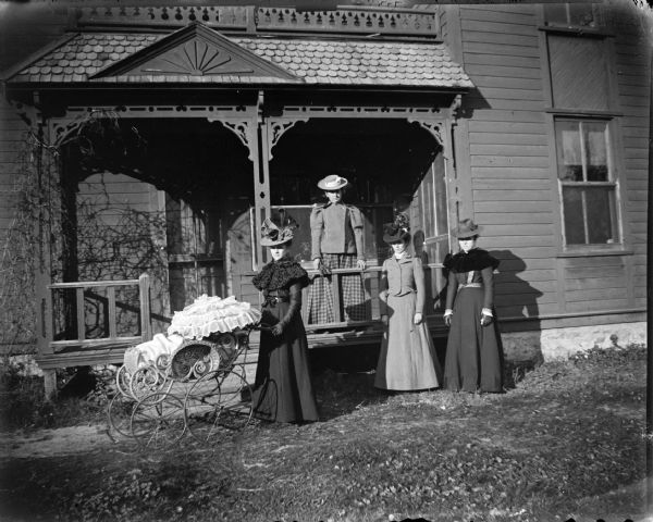 Four women posing in front of a frame house with a baby buggy.