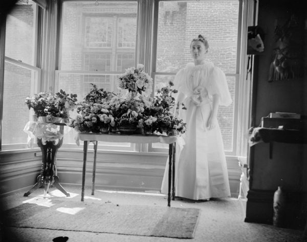 Woman, probably Edna Richards Turner, posing with her potted plants. The Methodist Church is in the background.