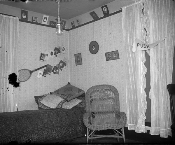 Interior of a bedroom with a bed, wicker chair, and walls displaying a tennis racquet and photographs.