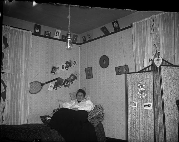Woman lying on a bed, walls displaying a tennis racquet and photographs.