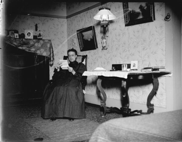 Woman reading a letter by a table.