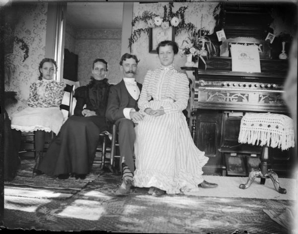 Three women and one man posed next to an organ. One woman sitting on the man's lap.
