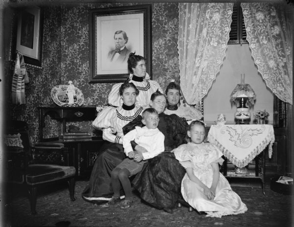 Four women, one elderly, and two children, probably Julia Spaulding and family. Spaulding twins, Julia, elderly woman, Sadie and children, Dudley and Marguerite (later Clausen) Osborn, posing in a parlor. Portrait on the wall may be of W.T. Price.