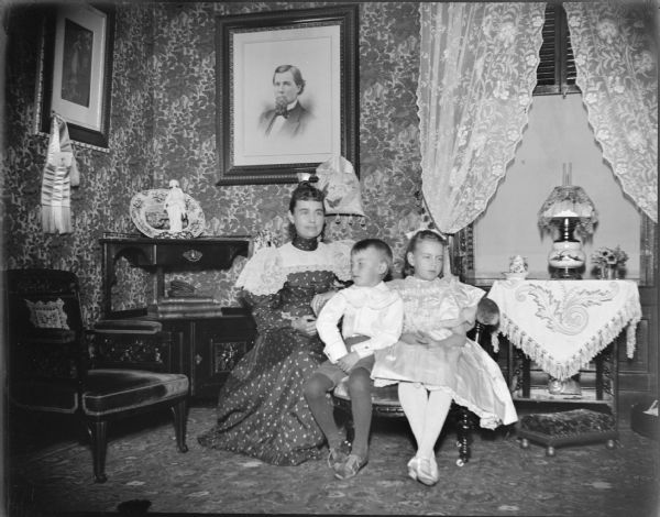Woman, probably Julia Spaulding Osborn, and two children, probably Dudley and Marguerite (later Clausen) Osborn, posing in the parlor inside the Spaulding House. Portrait on the wall may be of W.T. Price.