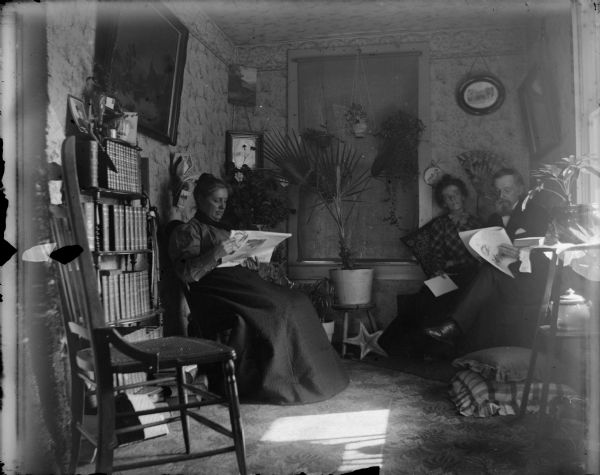 Two women and an elderly man reading in a room.