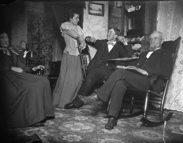 Two women and two men, both young and elderly, reading and conversing in a parlor, probably Mr. and Mrs. J.R. Ogden, and their son and daughter, Carl and Grace.