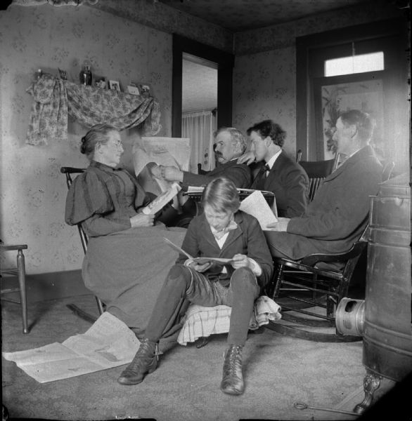 Three men, woman, and boy posed reading in a room.