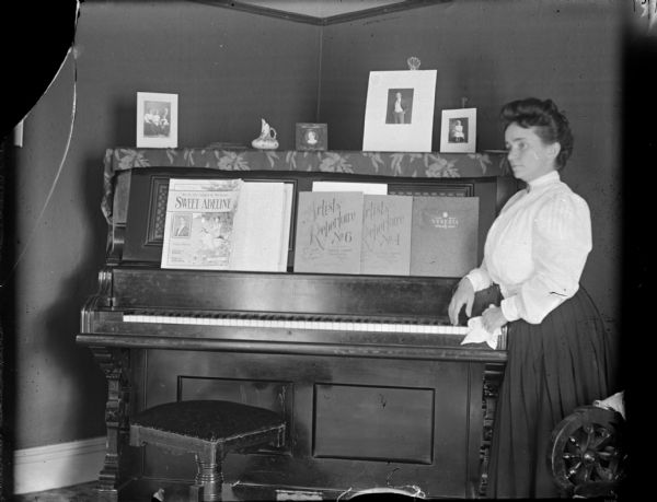 Woman posing next to a piano, probably Mrs. Merlin Hull, formerly Jessie Matchette.