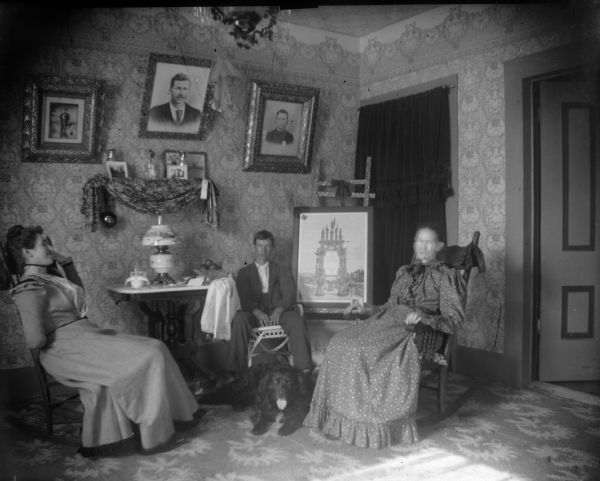 Two women, a man, and a dog sit in a parlor.