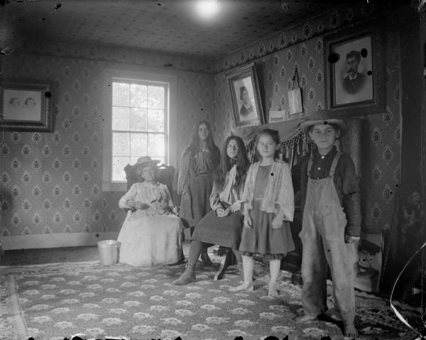 Woman sitting with three girls and one boy in a room, probably a farm family.