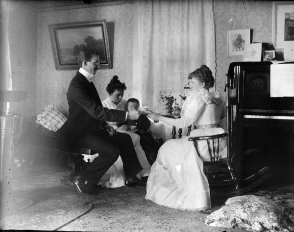 Two women, man, and child having tea in a parlor.