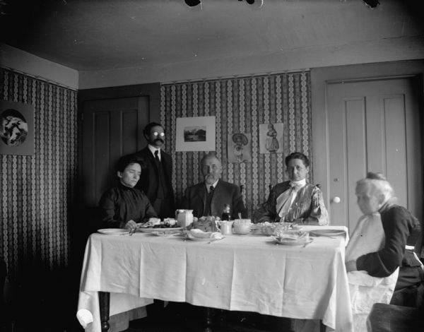 Two men and three women sitting down to a meal, possibly Mr. and Mrs. Merlin Hull on the left, and Mr. and Mrs. George Hull on the right, father and son.
