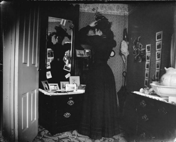 Woman putting on a hat in front of a dressing table mirror.