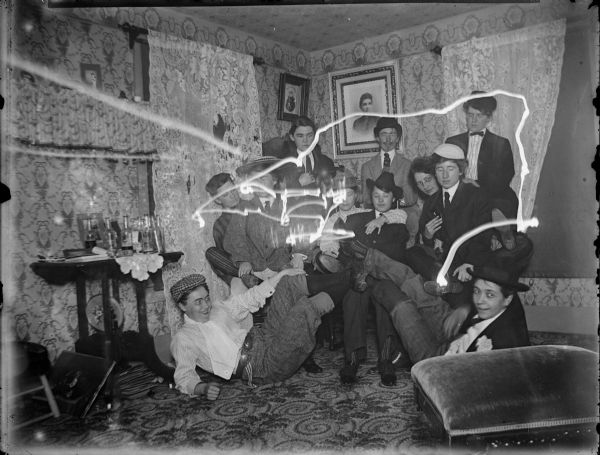 Large group of women dressed in men's clothing, some with their feet in the air, and several liquor bottles on the table. Overexposed light streaks also throughout the image.
