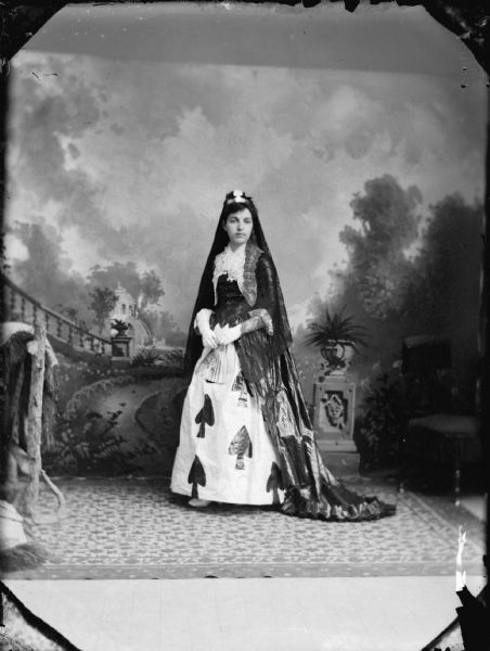Studio portrait of a woman dressed as the queen of spades, probably Minnie Jones Taylor, in front of a painted backdrop.