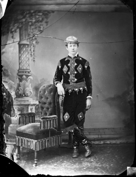 Studio portrait of a man, probably in circus costume posing in front of a painted backdrop.