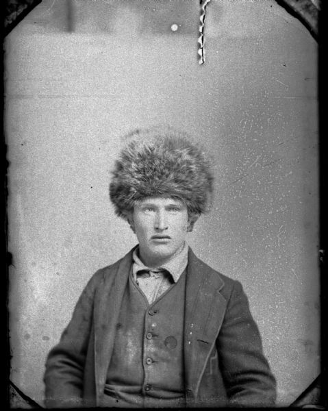 Studio portrait of a seated man wearing a fur hat, suit jacket, and vest. Possibly Frank Goodenough.