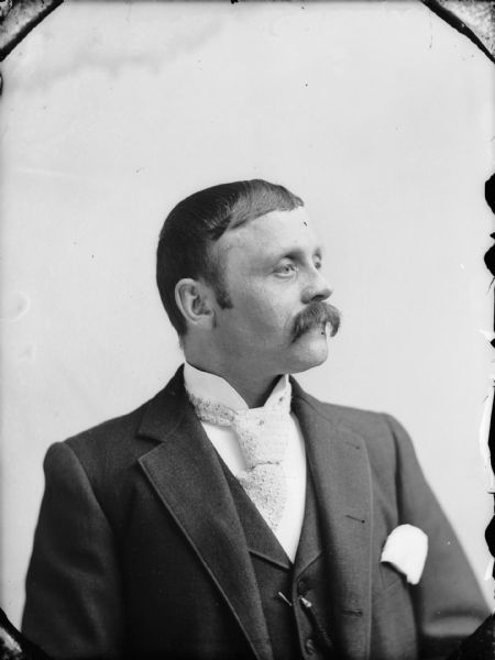 Studio portrait of a seated man with a moustache, wearing a large white necktie, with a vest, and suit jacket. Probably Peter L. Moe, the owner of a hardware store at First and Main Streets.