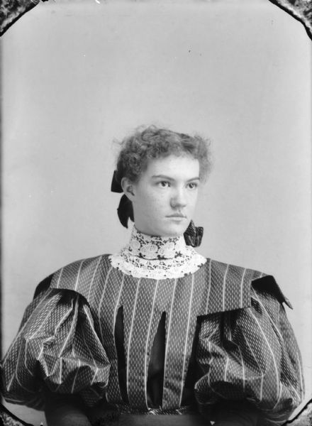 Studio portrait of a seated woman with a wide lace collar over a puffy-sleeved blouse, and a ribbon in her hair. Possibly Oce Thompson Lozier, the daughter of grocer W.J. Thompson.	

