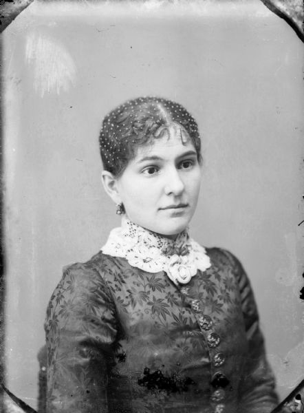 Studio portrait of a seated woman with netting over her hair and a flowered lace collar.