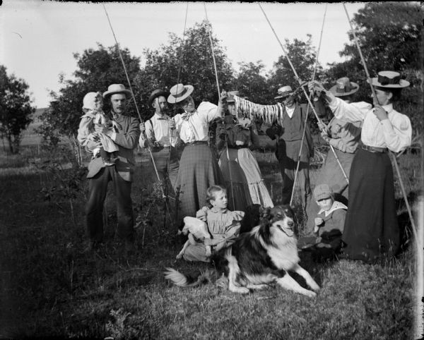 Group of three men, four women, two girls, one boy, and a dog displaying fish caught.