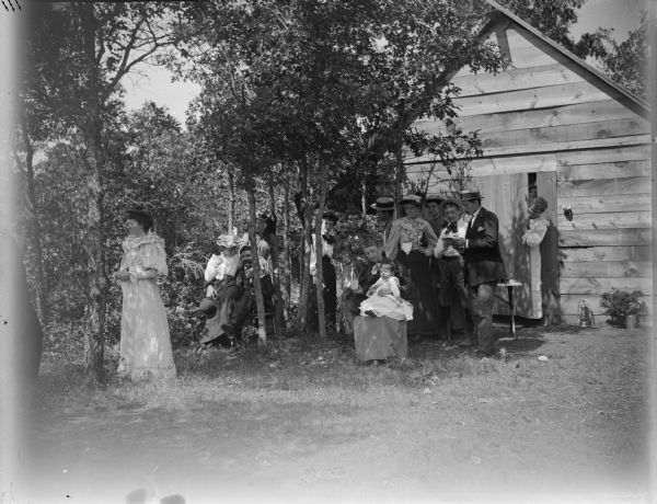 Large group posing outside a small cabin.