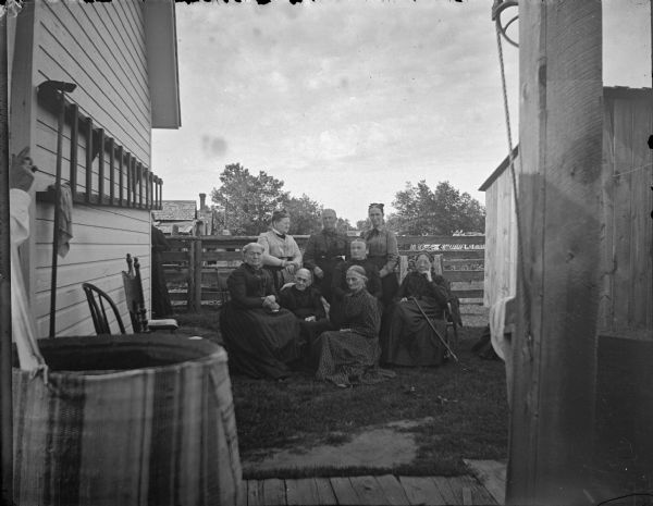 Eight elderly women posed between two buildings, probably a backyard.