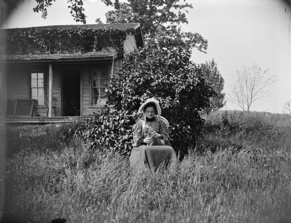 Woman sitting in a chair petting a cat in front of a house.