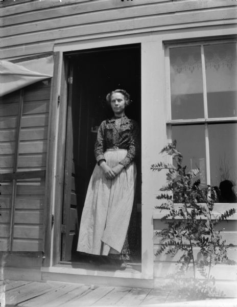 Woman posed standing in the doorway of a house.  