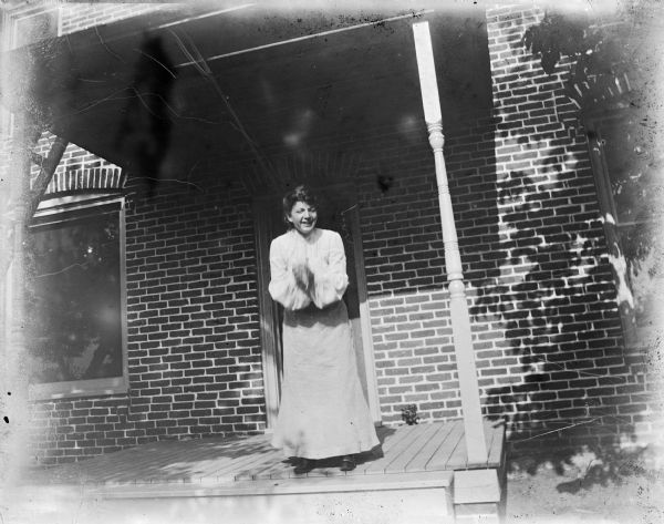 Woman standing on the wooden porch of a brick house moving her hands.