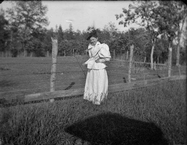 Woman posed standing by a barbed wire fence.	