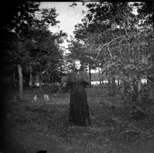 Woman posed standing among deciduous trees.