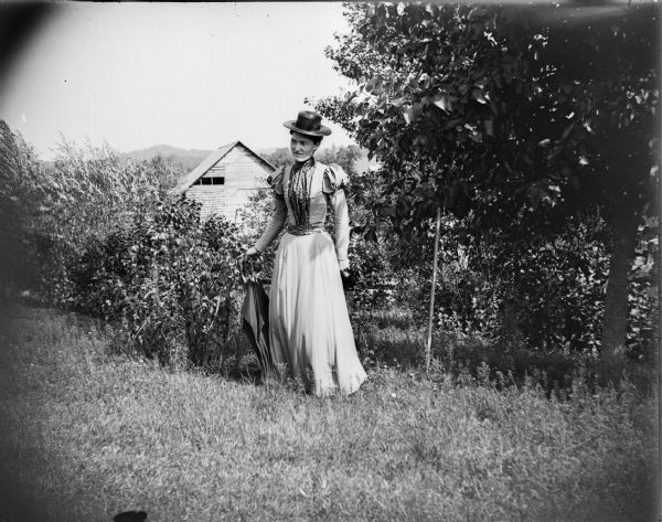 Woman posed standing with a folded umbrella by flowers.