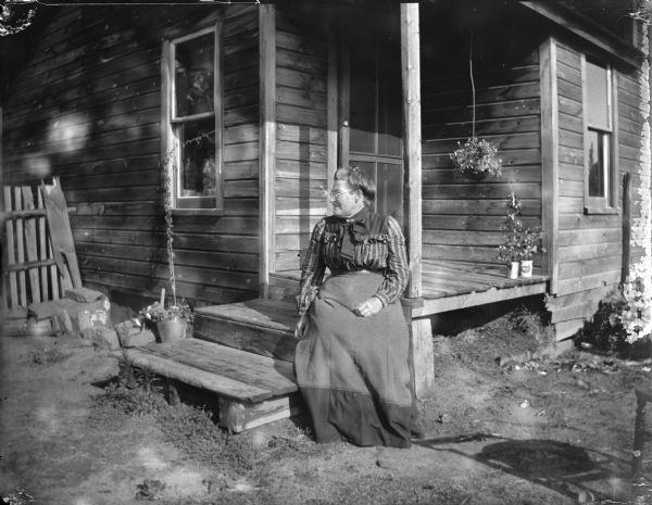 Elderly woman in a long skirt sitting on the front steps of a house.