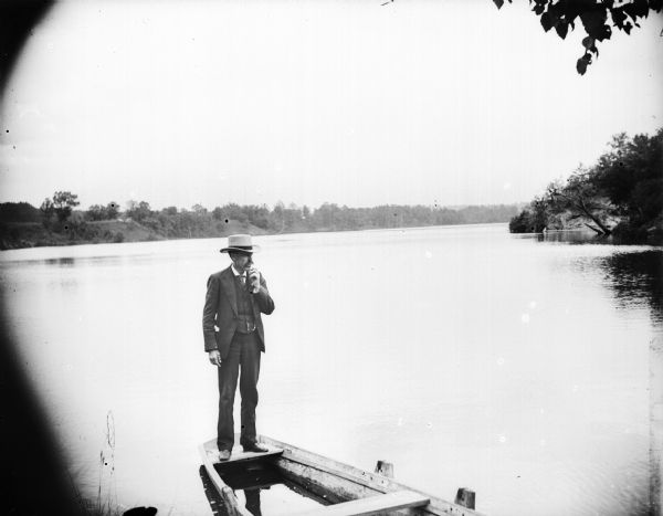 Man posed standing on the stern of a boat which is partially sunk in the river.