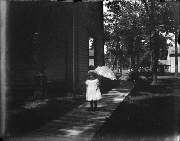 Small girl posed standing with a ruffled umbrella on a board sidewalk.
