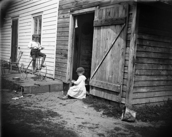 A small girl sits pounding with a hammer as a boy rides a tricycle.	
