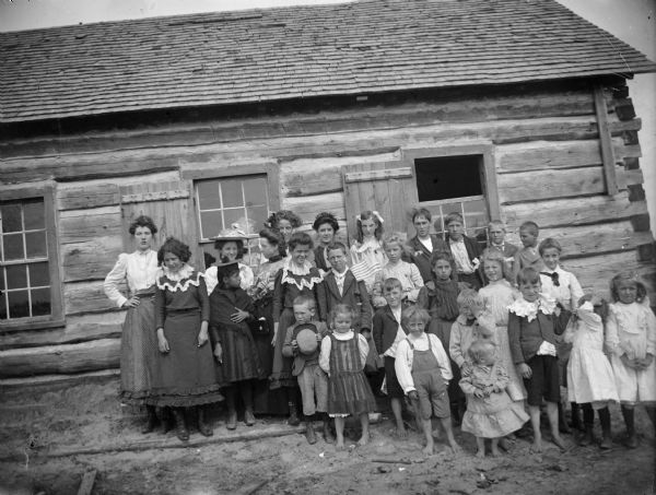 A group of children pose in front of a log building.