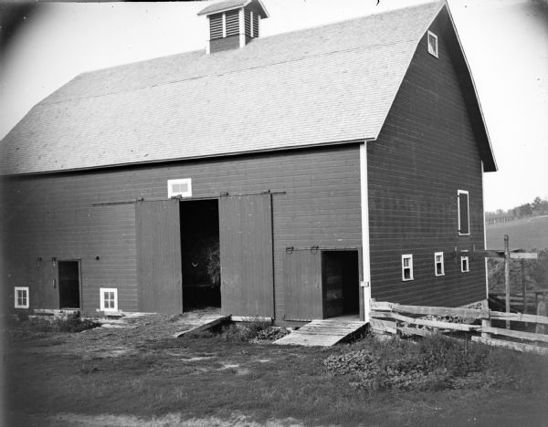 A barn with three open doors. Through the main door to the barn, hay is visible.