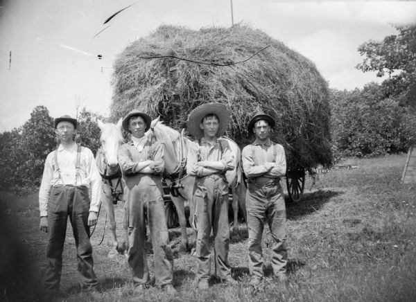 Four men stand in front of a hay wagon that is pulled by a two-horse team. One of these men could be H. John Dietrich.
