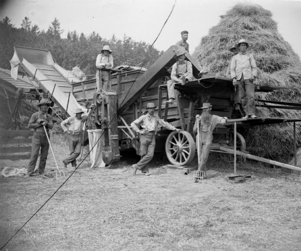 A group of eight farmers resting on or near a wooden threshing machine.