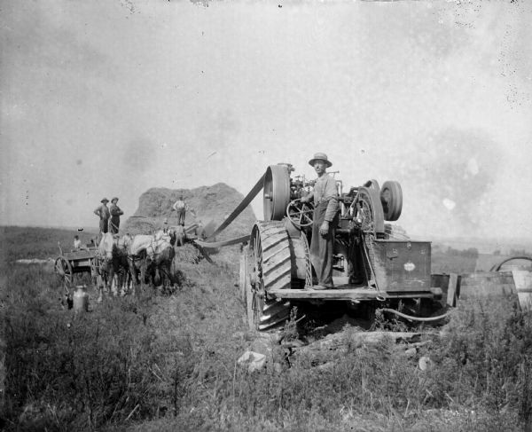 A crew works with a steam tractor and threshing machinery in a field.