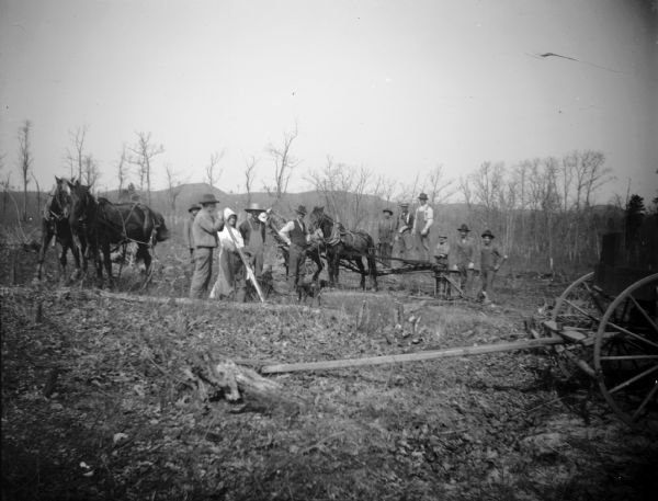 A group of men and women stand in a field with a stump extracting rig.
