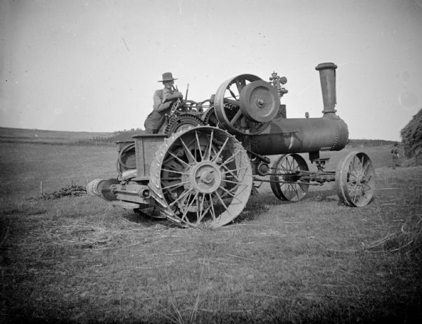 A farmer leans on a steam tractor in a field.