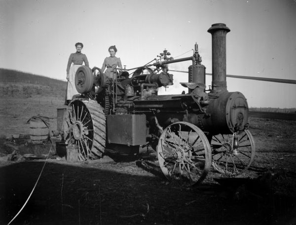Two women pose standing on a steam tractor.