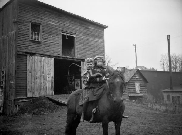 Two girls are riding a horse bareback in a farmyard.