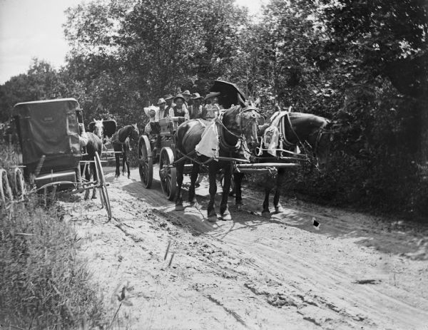 A crowded wagon pulled by a team of two horses meets other buggies on a country road.	
