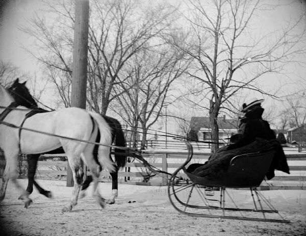 Winter scene with a man and woman sitting in a cutter sleigh pulled by a two-horse team, possibly driven by Harvey Risliands.	