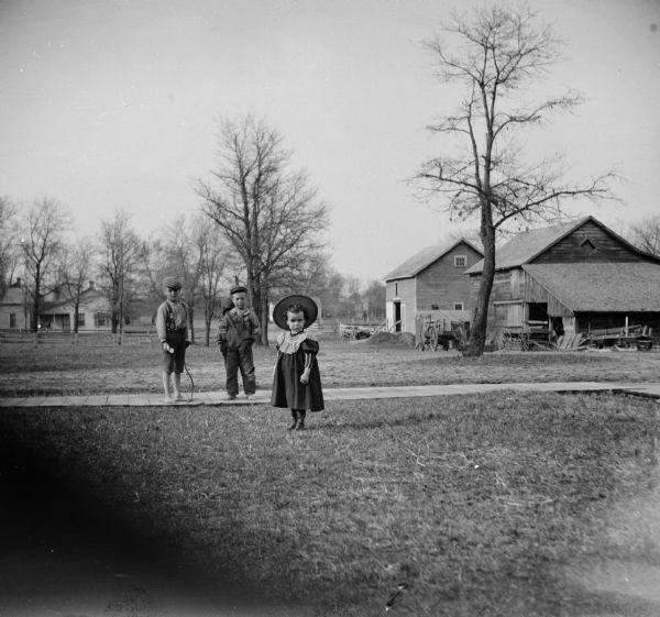 Four children play outside in a yard. One of the children hides behind another and is hardly visible.