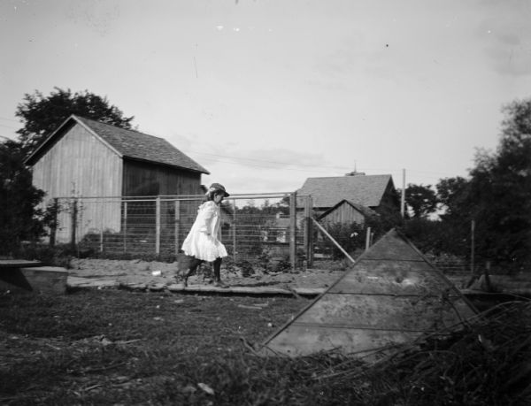 A young girl runs along a boardwalk through a farm yard.
